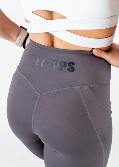 Chest to Thigh 3/4 Back View with Hands on Sides Wearing Empowered Leggings x FIT OPS | Grey